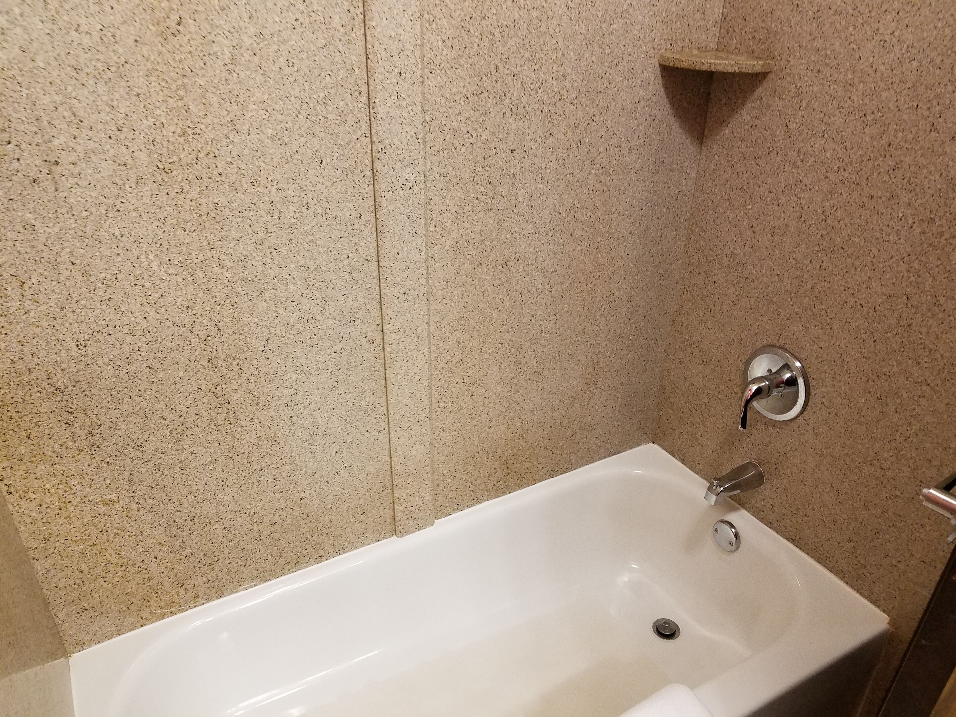 A bathroom with a white bathtub, a wall-mounted faucet, and a small shelf above the tub.