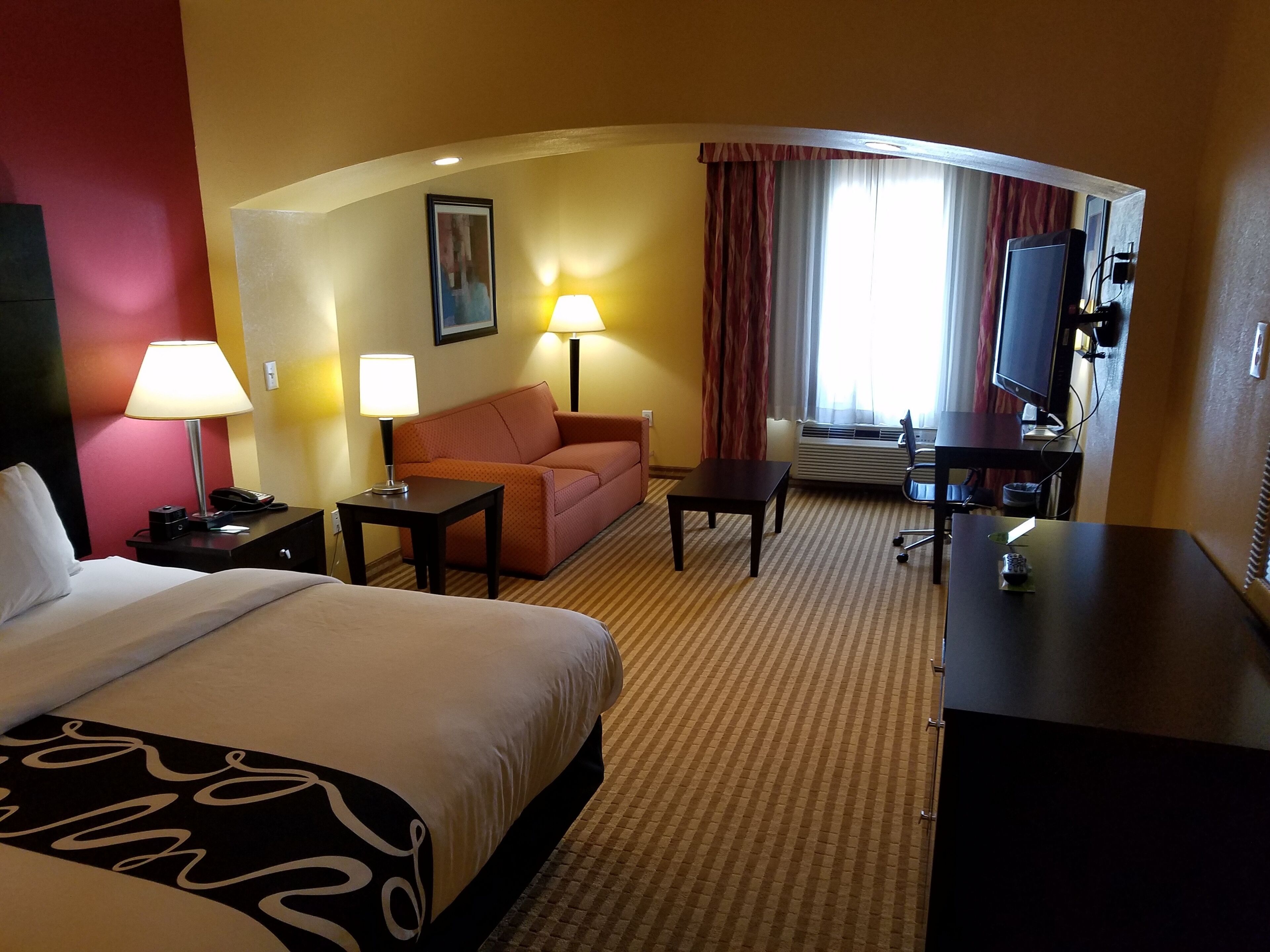 A hotel room with a bed, a sofa, a desk, a TV, and a lamp.
