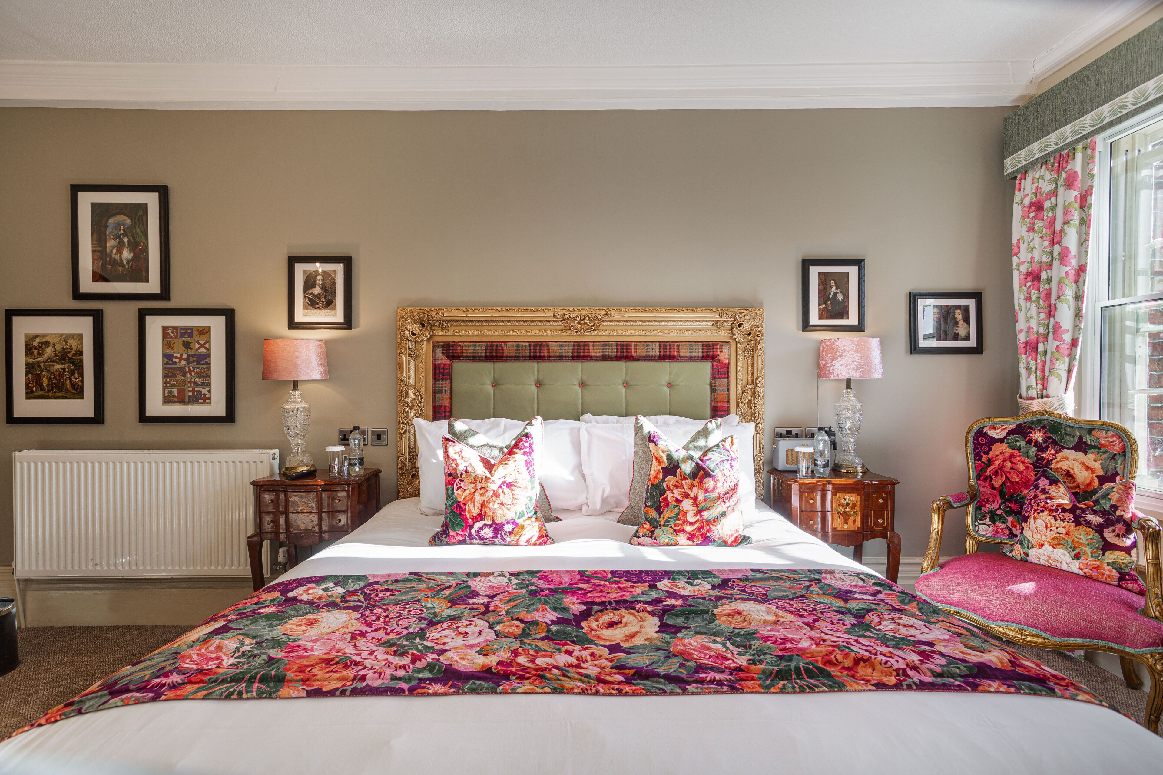 A bedroom with a large bed, a headboard, a floral-patterned bedspread, and a chair with a floral upholstery.