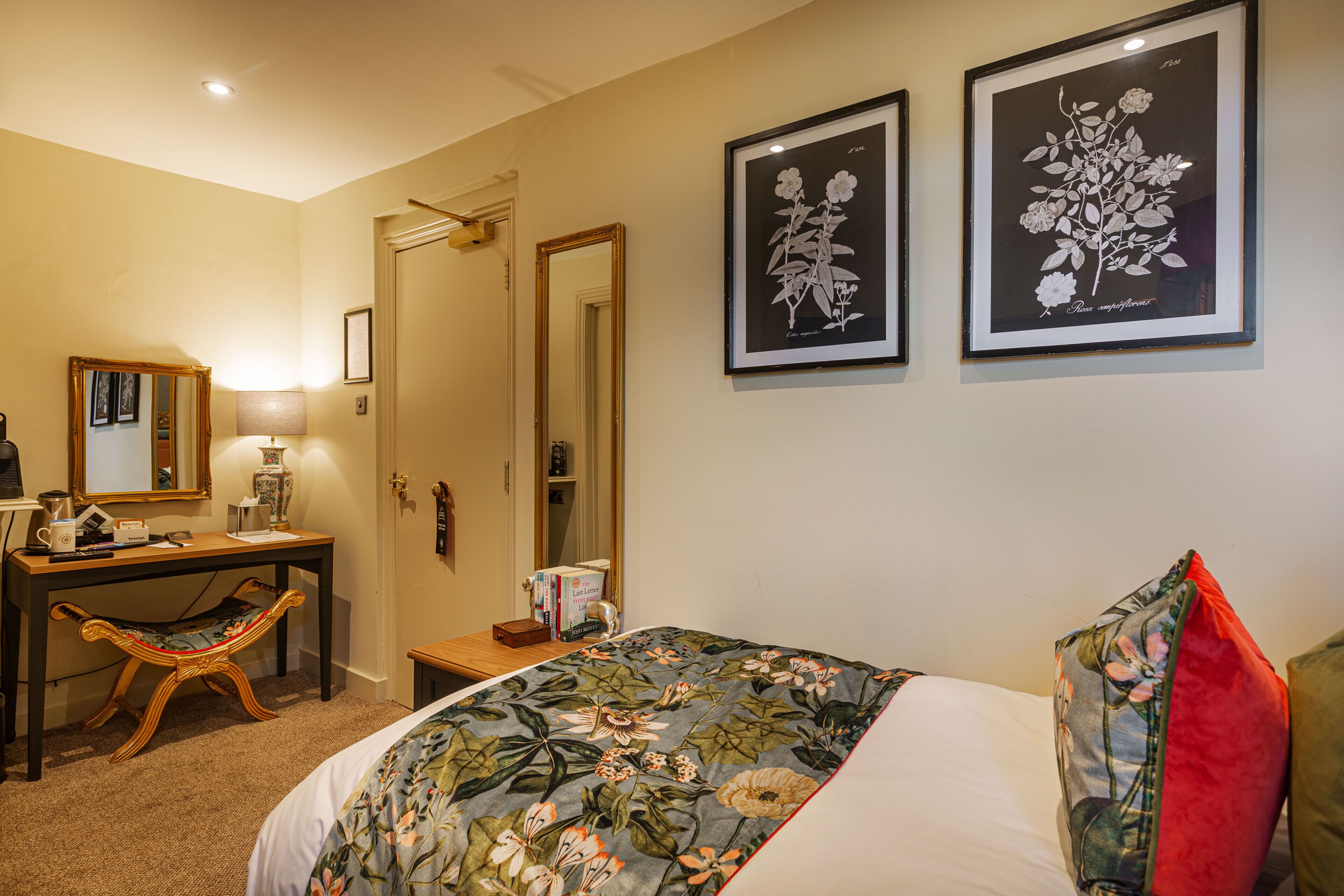 A bedroom with a bed, a desk, a chair, and two framed botanical prints on the wall.