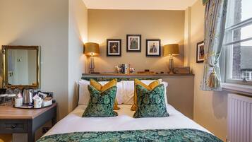 A hotel room with a bed, bedside table, lamp, framed pictures, and a window with curtains.