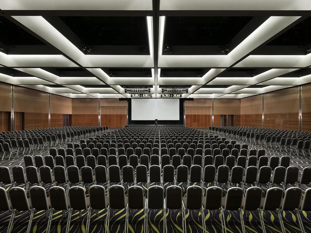 A conference room with rows of chairs, a large screen at the front, and a modern ceiling design.