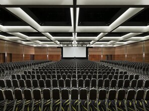 A conference room with rows of chairs, a large screen at the front, and a modern ceiling design. - Crown Promenade Perth (Perth)