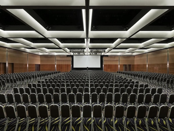 Un salón de conferencias con filas de sillas, una pantalla grande al frente y un diseño de techo moderno.