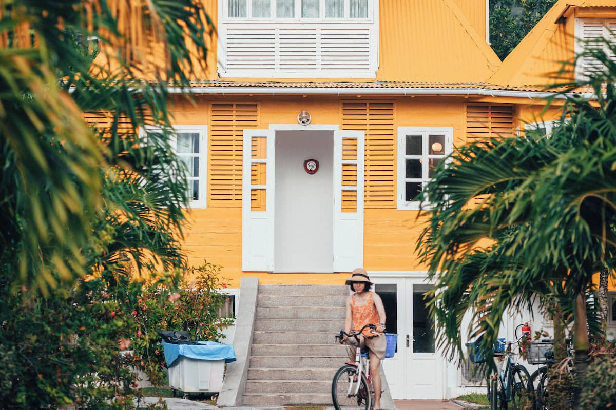 Una casa amarilla con una escalera que lleva a la entrada, rodeada de follaje.