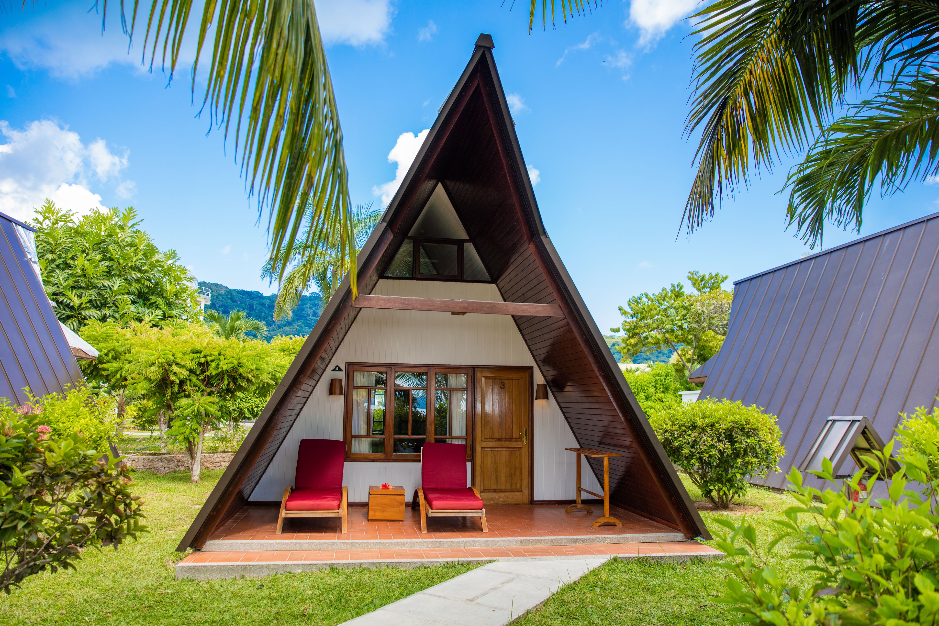 A triangular-shaped building with a balcony, red chairs, and a wooden table.