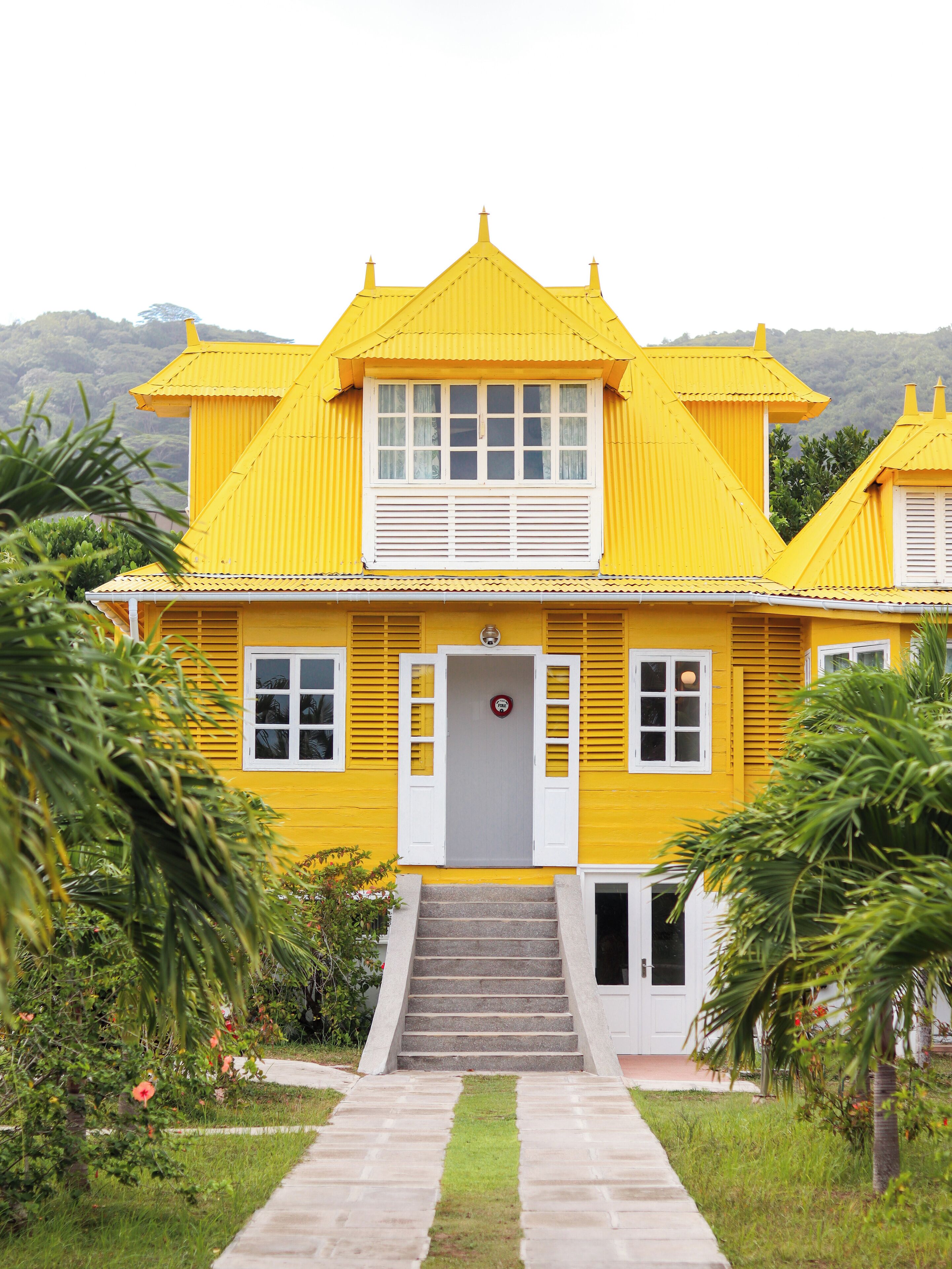 Un bâtiment jaune avec un escalier menant à l’entrée, entouré de verdure.