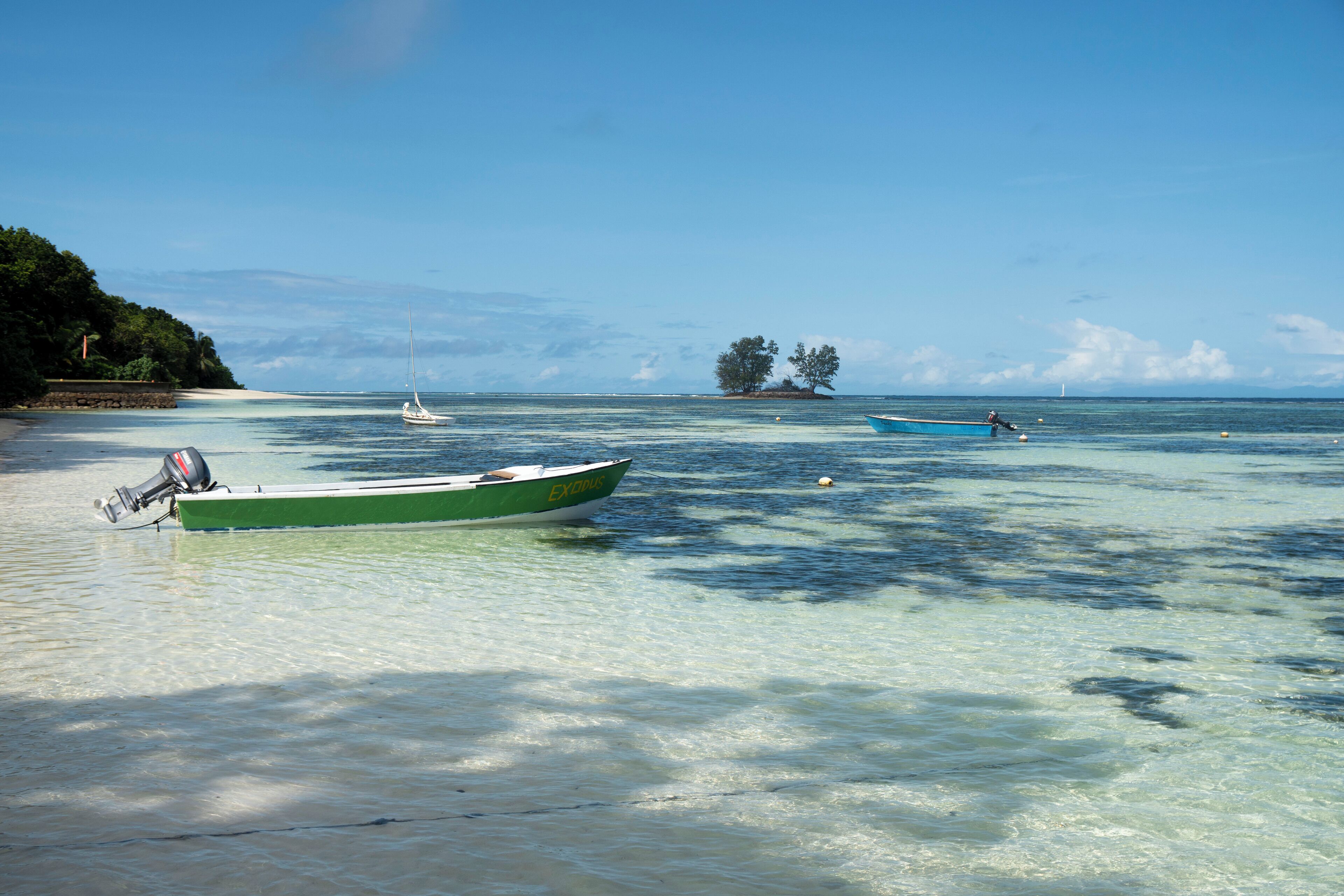 A calm beach with clear waters, a green boat, and a distant island.