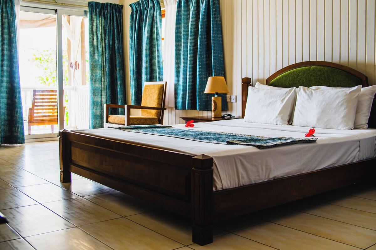 A hotel room with a wooden bed, a chair, a lamp, and a view of the outdoors through a sliding door.