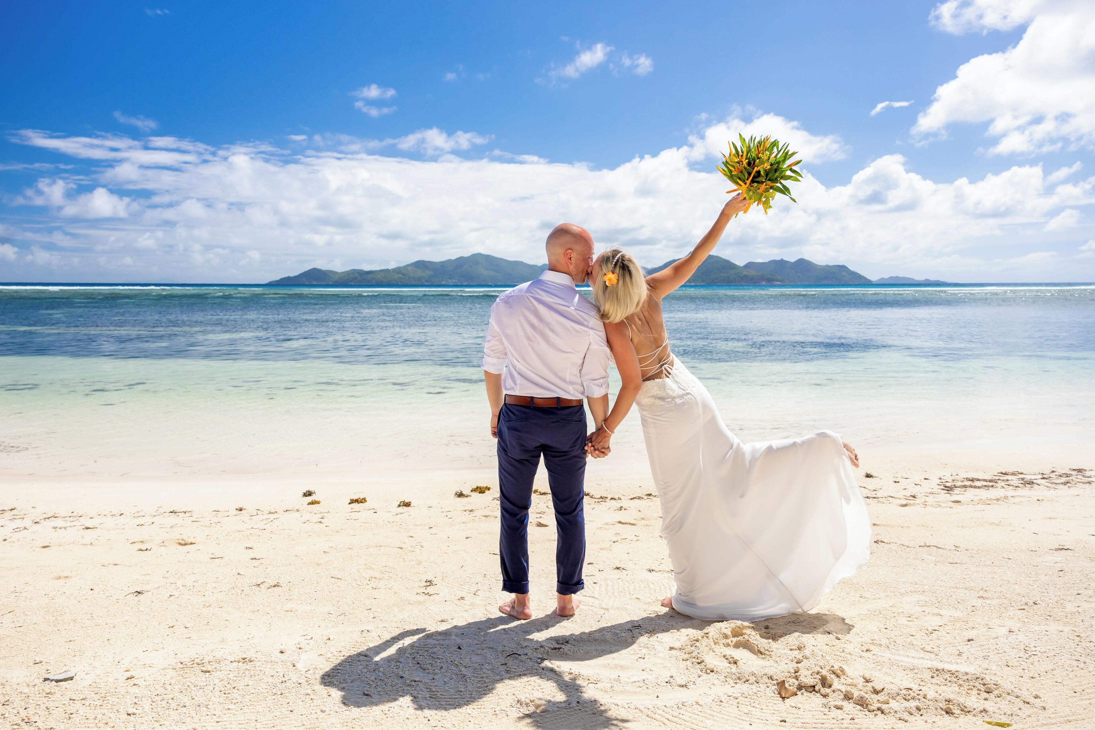 Una pareja en una playa con agua cristalina y montañas al fondo.