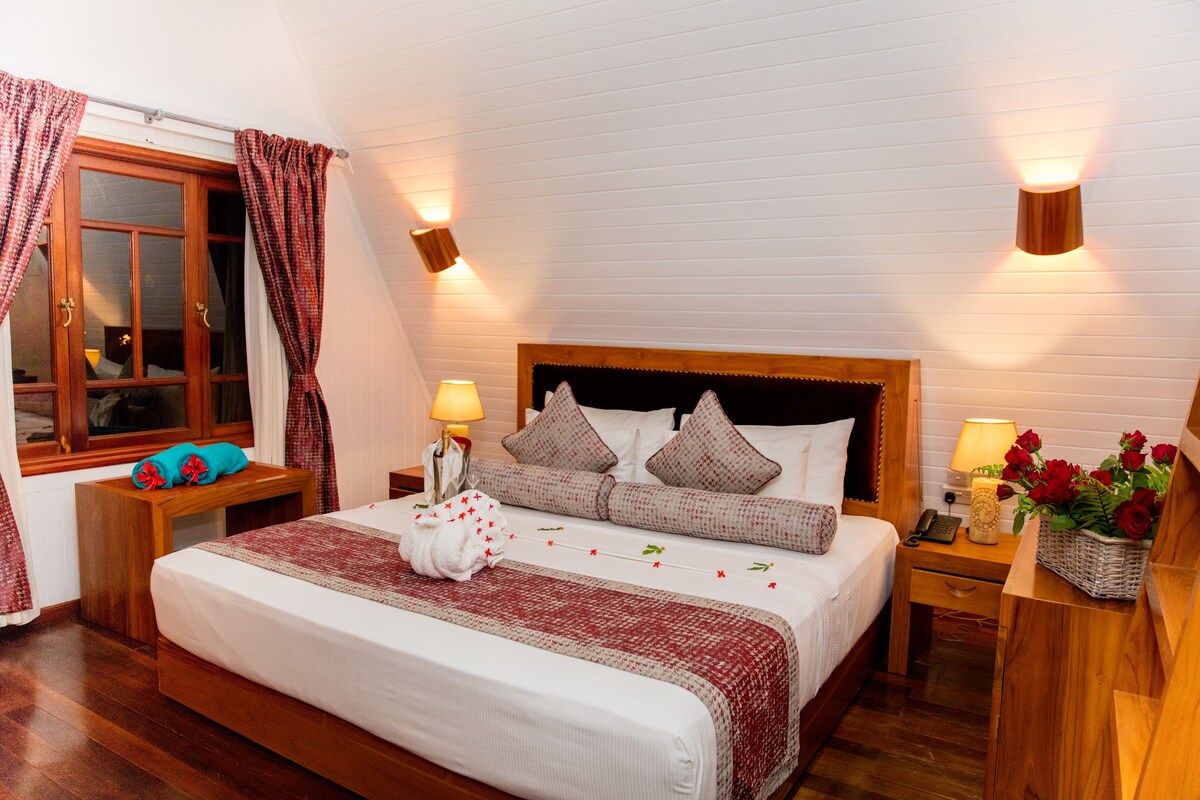Un dormitorio ordenado con una cama grande, cabecera de madera, mesitas de noche con lámparas y una ventana con cortinas.