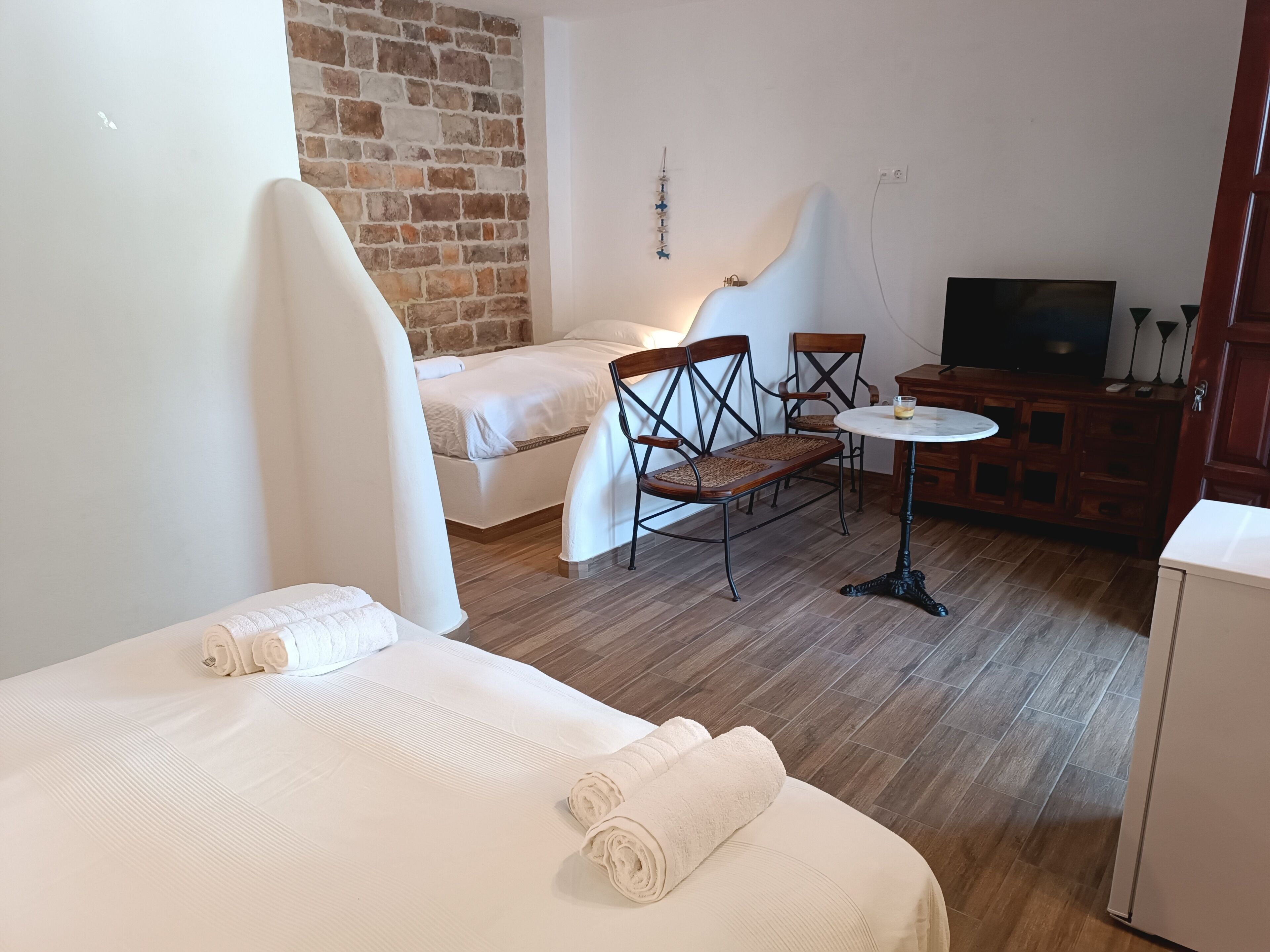 Una habitación de hotel con cama, una mesita con sillas, televisión y pared de ladrillo.