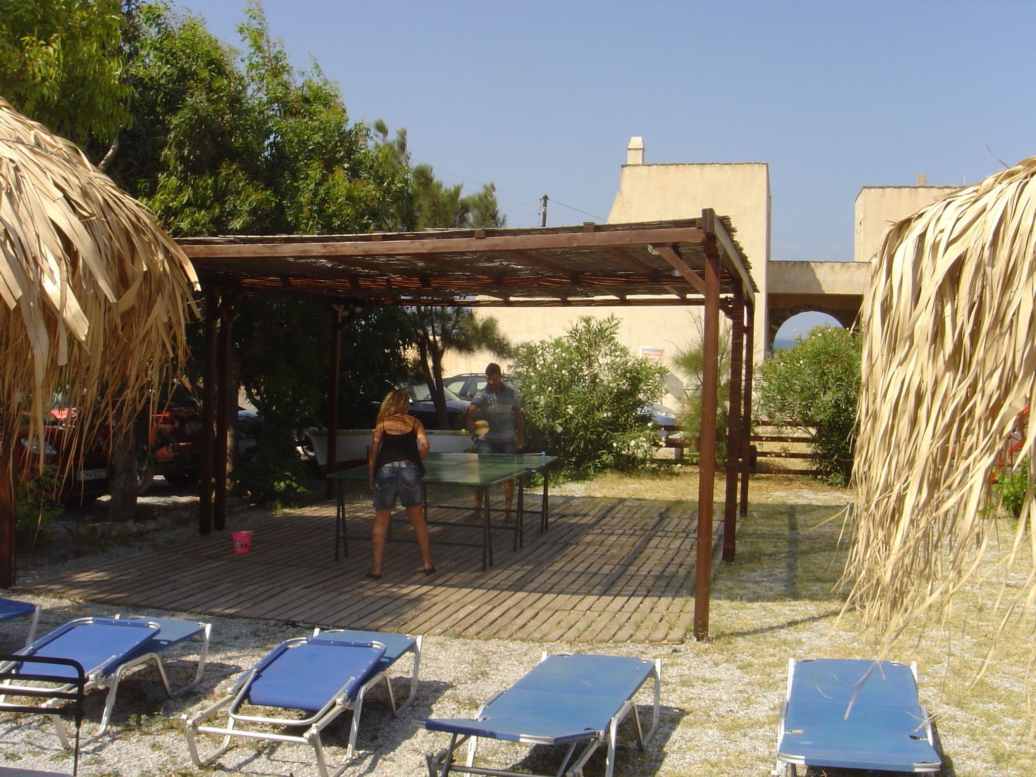 A covered outdoor area with a table and chairs, surrounded by lounge chairs and a pergola.