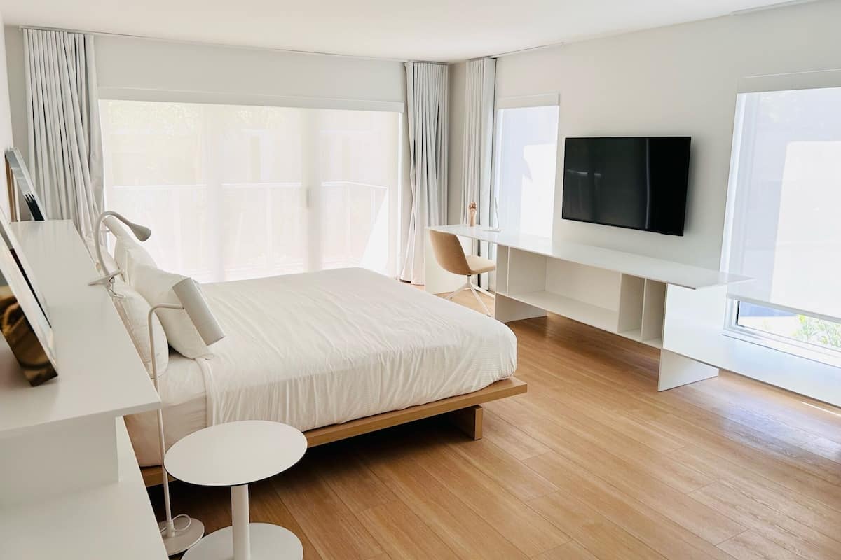 A modern hotel bedroom with a large bed, a desk, a chair, and a TV.