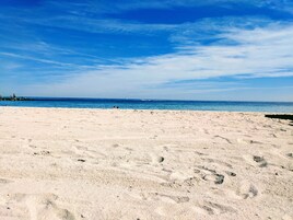 Una playa arenosa con huellas, un cielo azul despejado y el océano al fondo.