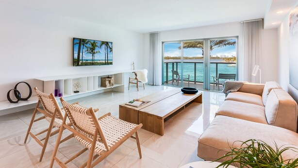 A modern living room with a sofa, coffee table, and wicker chairs. A large window offers a view of the sea. - Beach Haus Bal Harbour (Bal Harbour)