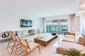 A modern living room with a sofa, coffee table, and wicker chairs. A large window offers a view of the sea. - Beach Haus Bal Harbour (Bal Harbour)