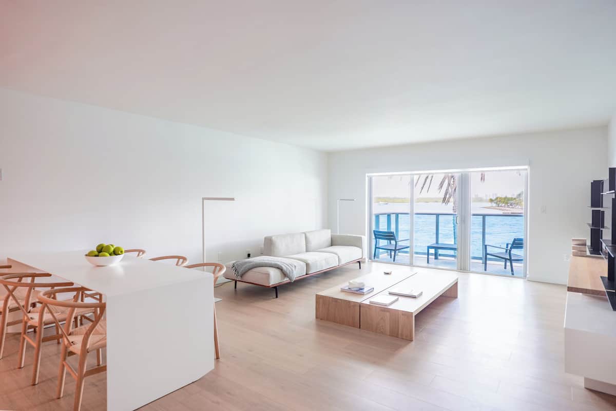 A modern living room with a white sofa, wooden coffee table, and a dining area with chairs and a white table.