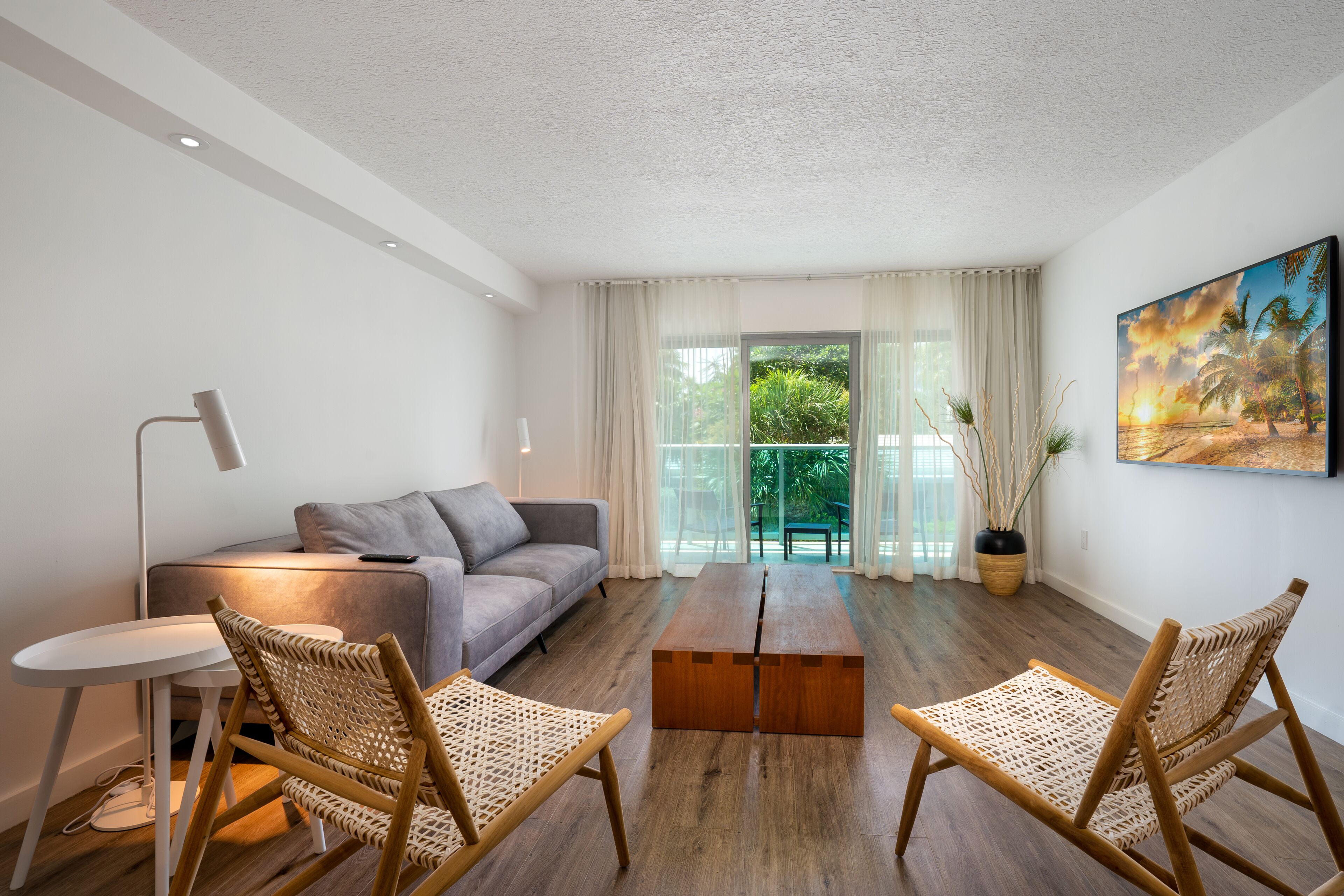 Una sala de estar moderna con un sofá gris, dos sillas de mimbre, una mesa de centro de madera y una lámpara de pie.