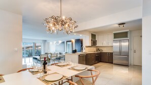 A modern kitchen with stainless steel appliances, a dining area with a chandelier, and a view of the cityscape. - Beach Haus Bal Harbour (Bal Harbour)