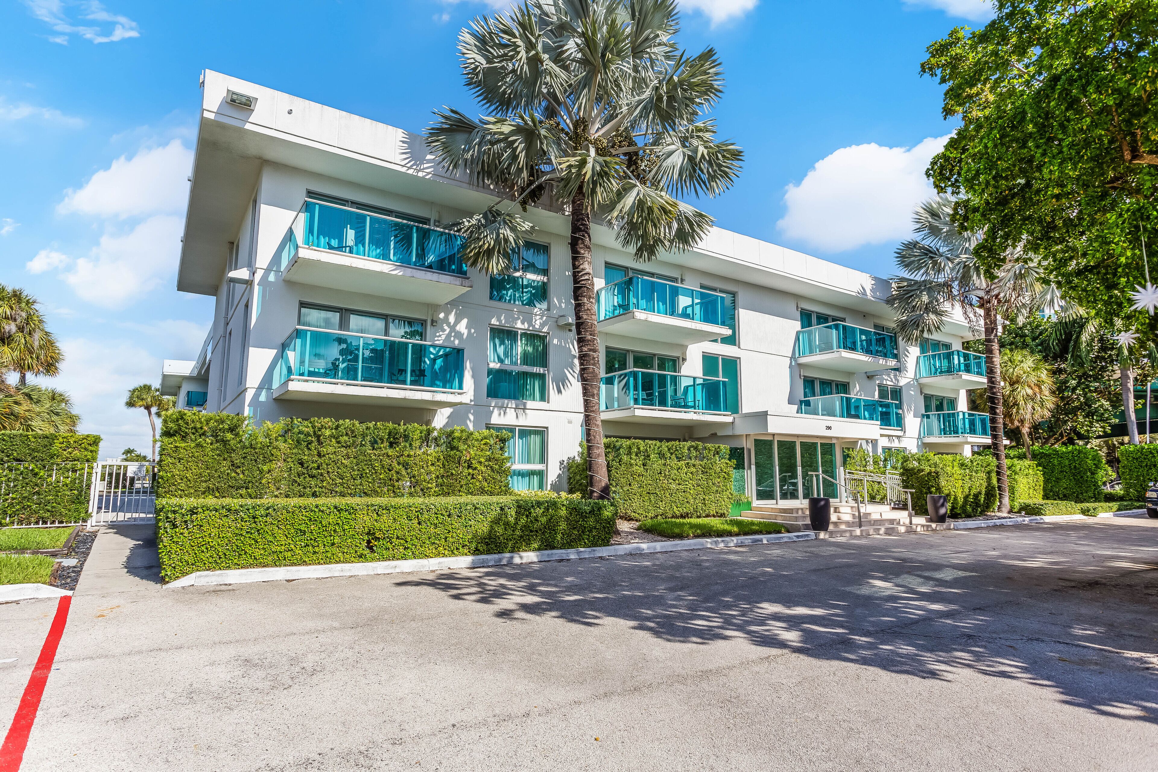 A modern multi-story hotel with balconies, palm trees, and well-maintained hedges.