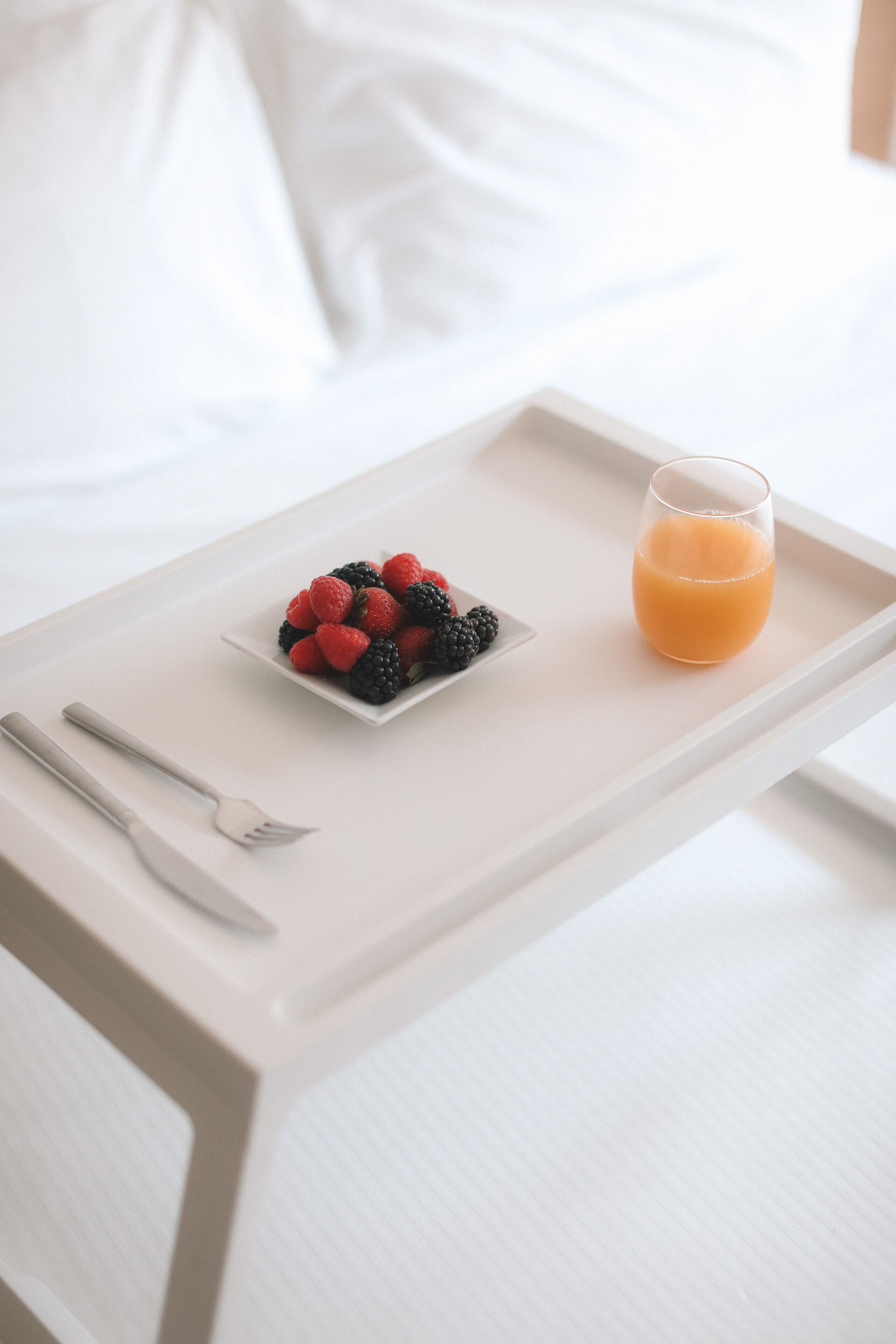 A tray with a glass of orange juice and a plate of berries on a bed.