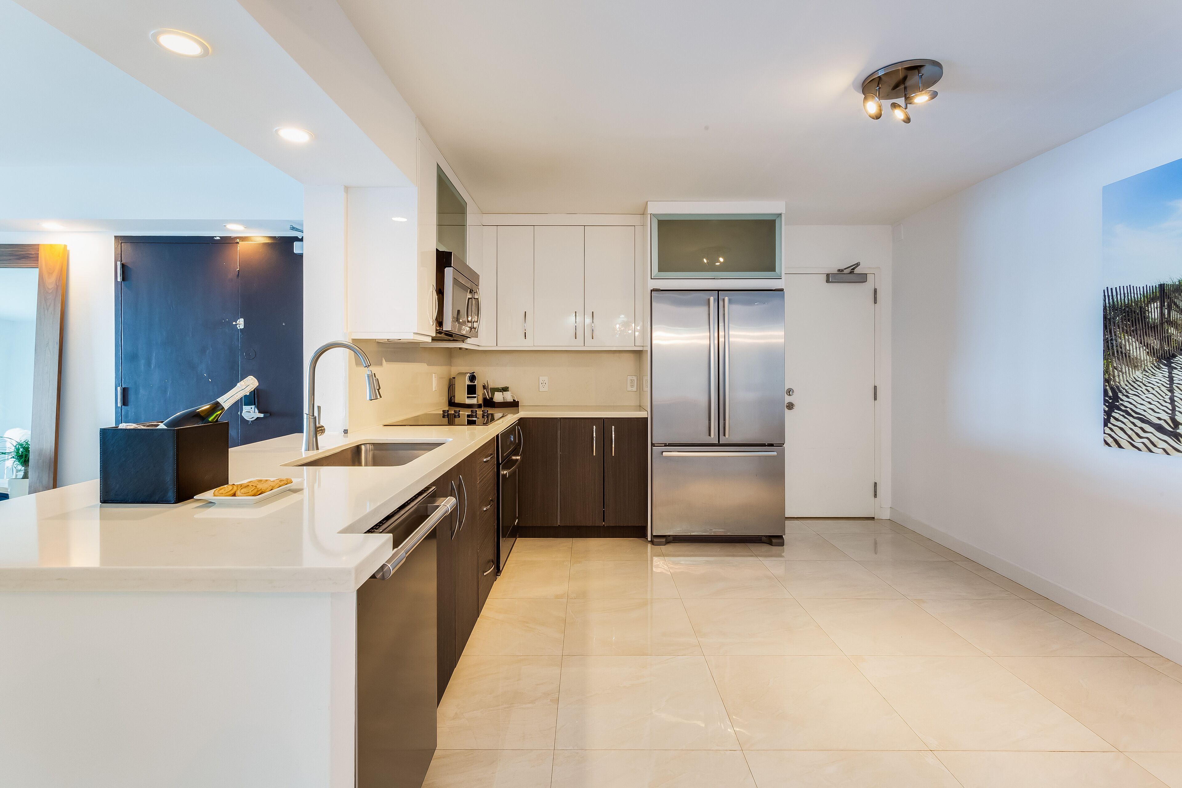 A modern kitchen with white countertops, dark cabinets, stainless steel appliances, and recessed ceiling lights.