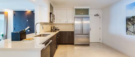 A modern kitchen with white countertops, dark cabinets, stainless steel appliances, and recessed ceiling lights.