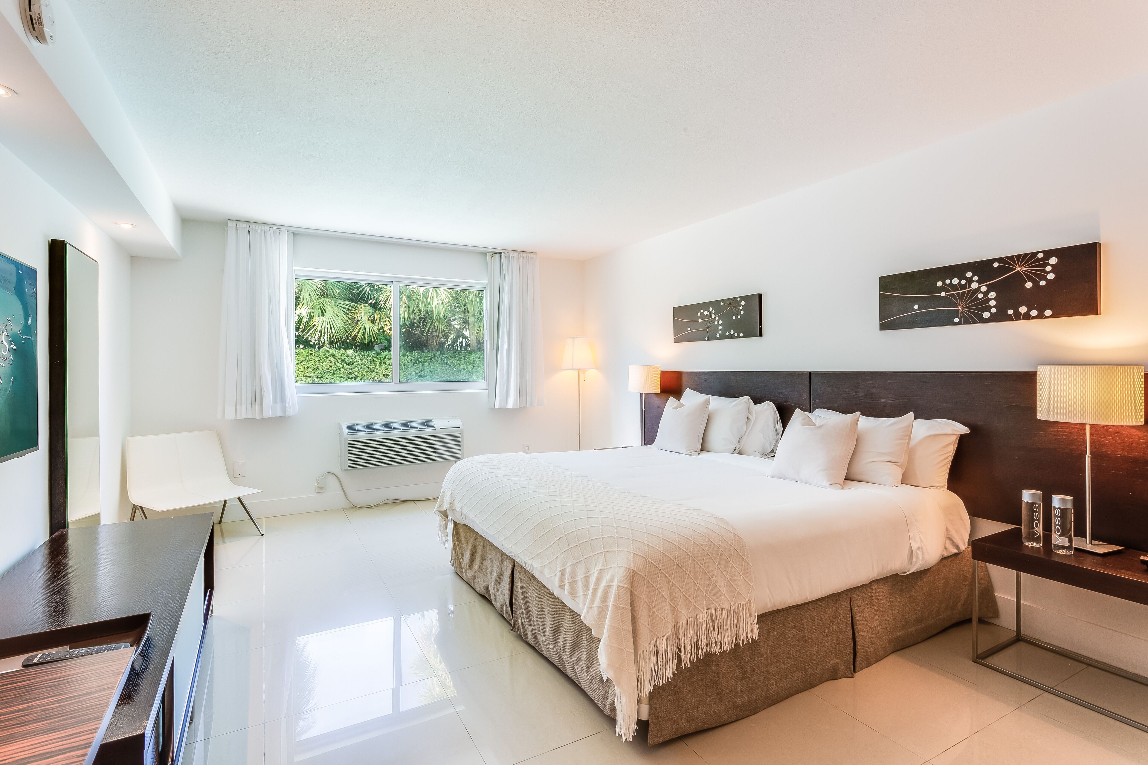 Ein modernes Hotelzimmer mit einem großen Bett, einem Schreibtisch und einem Stuhl. Es gibt ein Fenster mit Vorhängen, eine Wandlampe und eine Dekoration über dem Bett.