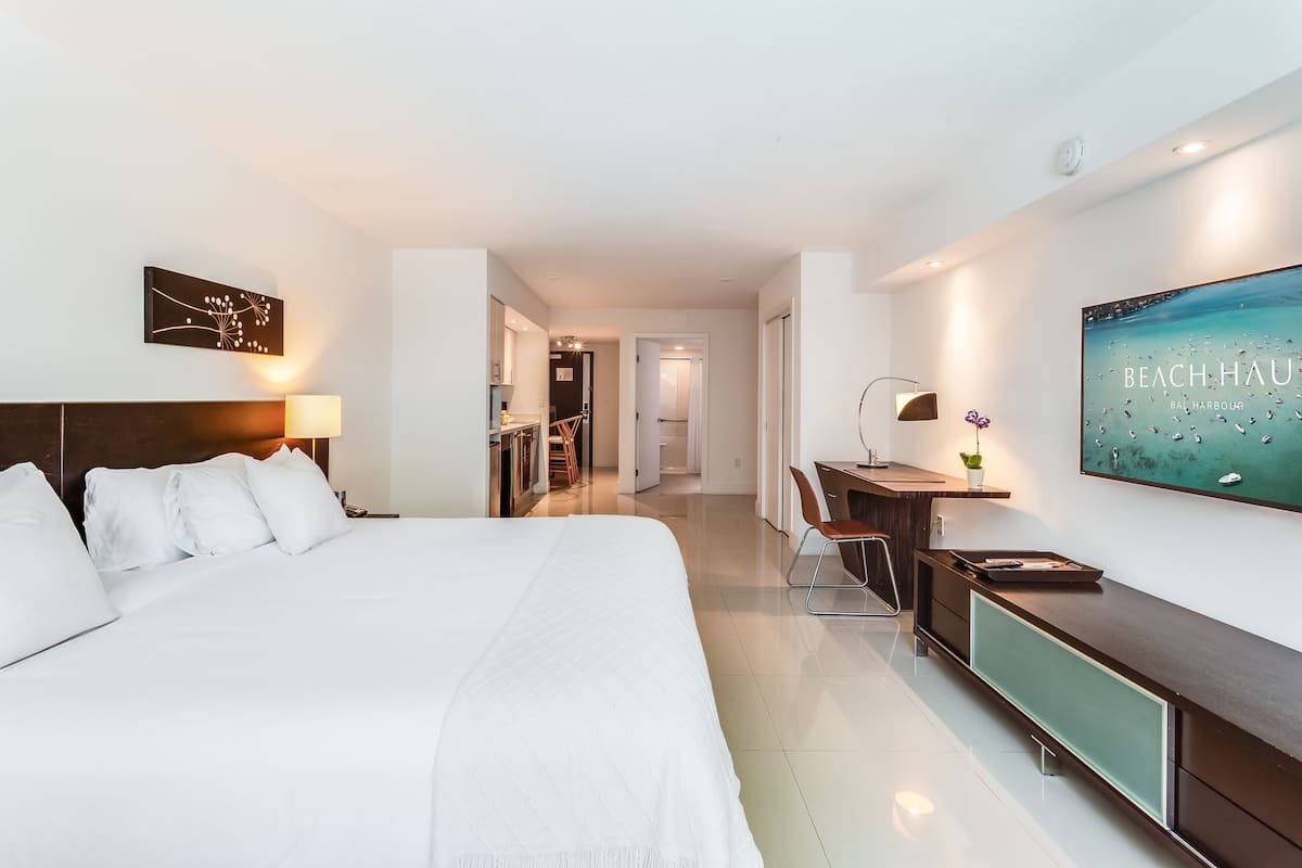 A modern hotel room with a large bed, a desk, and a view of the sea.