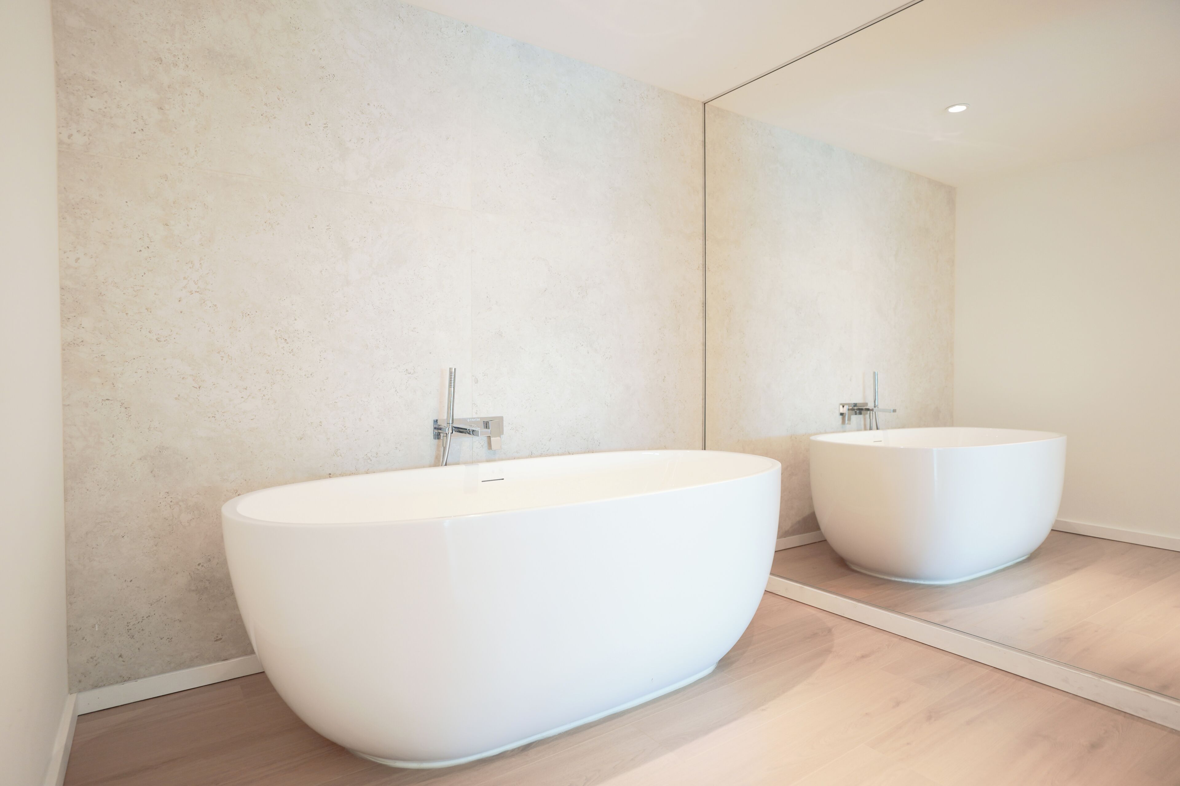 A modern bathroom with a large freestanding bathtub, a wall-mounted sink, and a large mirror reflecting the space.