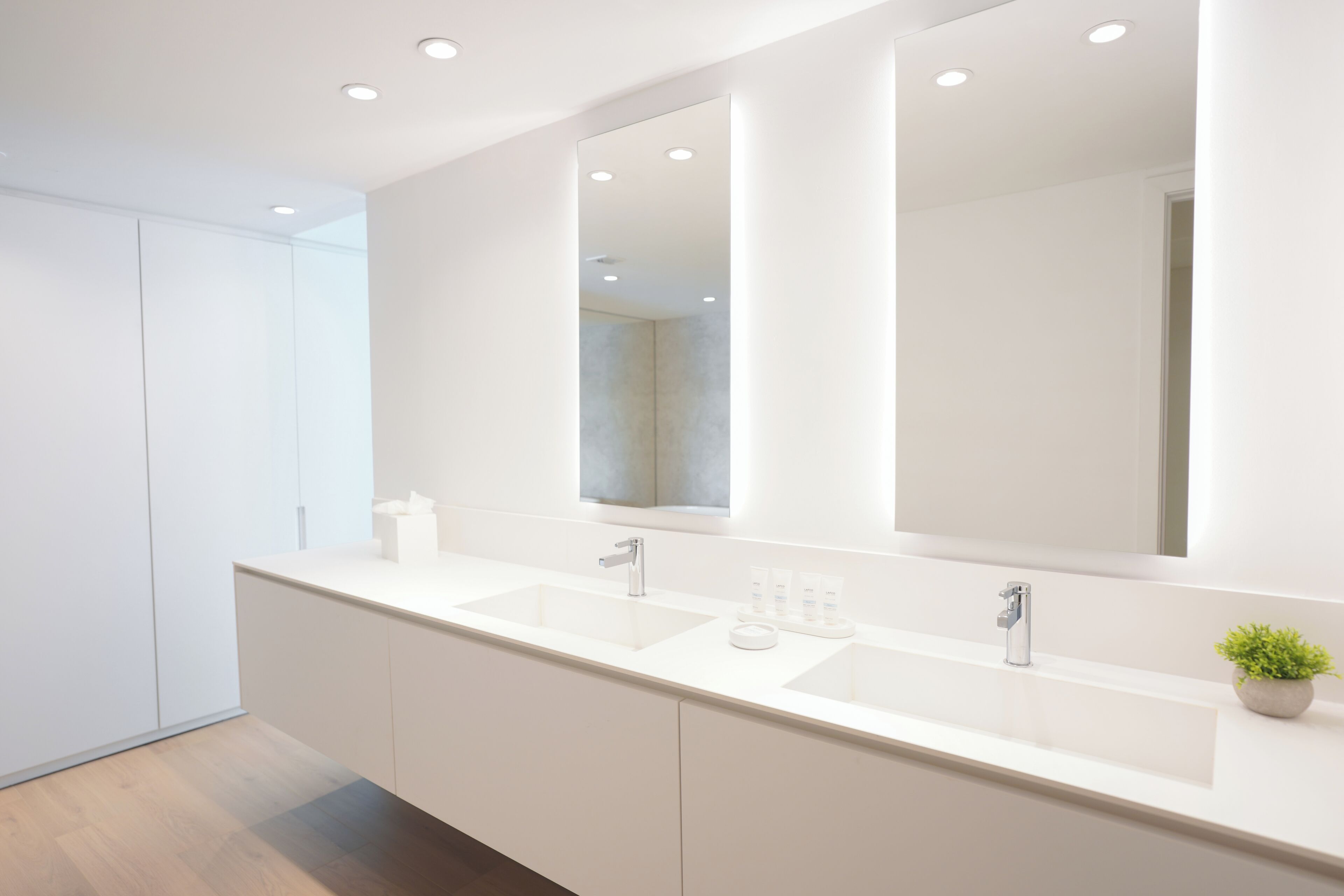 Un baño moderno con un espejo grande, dos lavamanos y una planta en maceta.