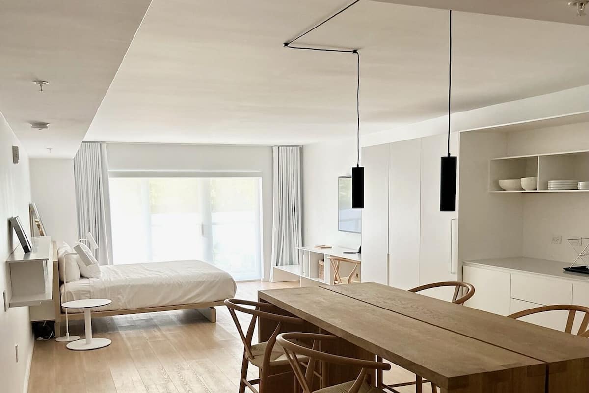 A modern, minimalist bedroom with a large bed, bedside tables, and a window with curtains.