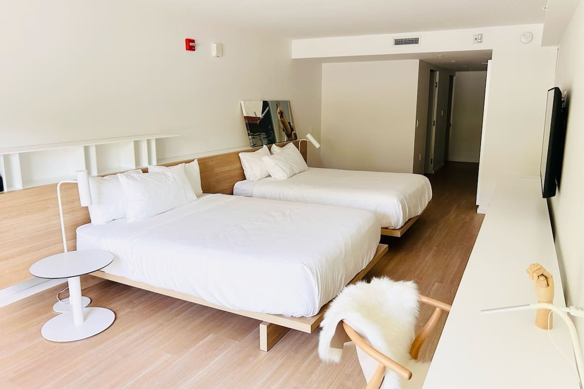 A modern hotel room with two single beds, a small round table, a chair, and a TV.