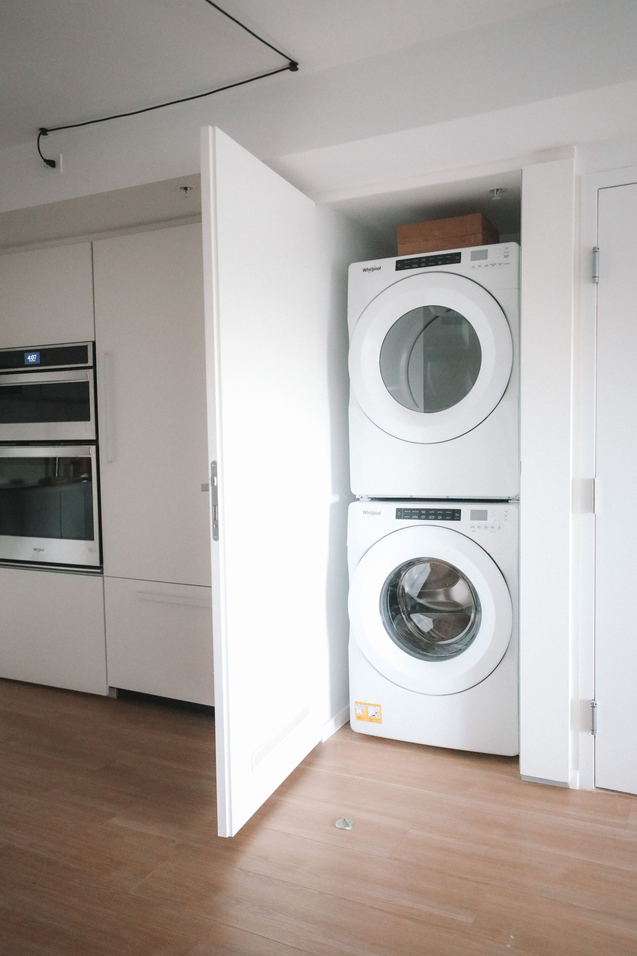 A laundry room with two stacked washers and dryers, a wooden floor, and white cabinetry.