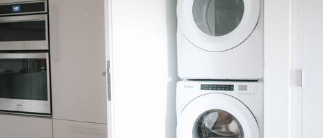 A laundry room with two stacked washers and dryers, a wooden floor, and white cabinetry.