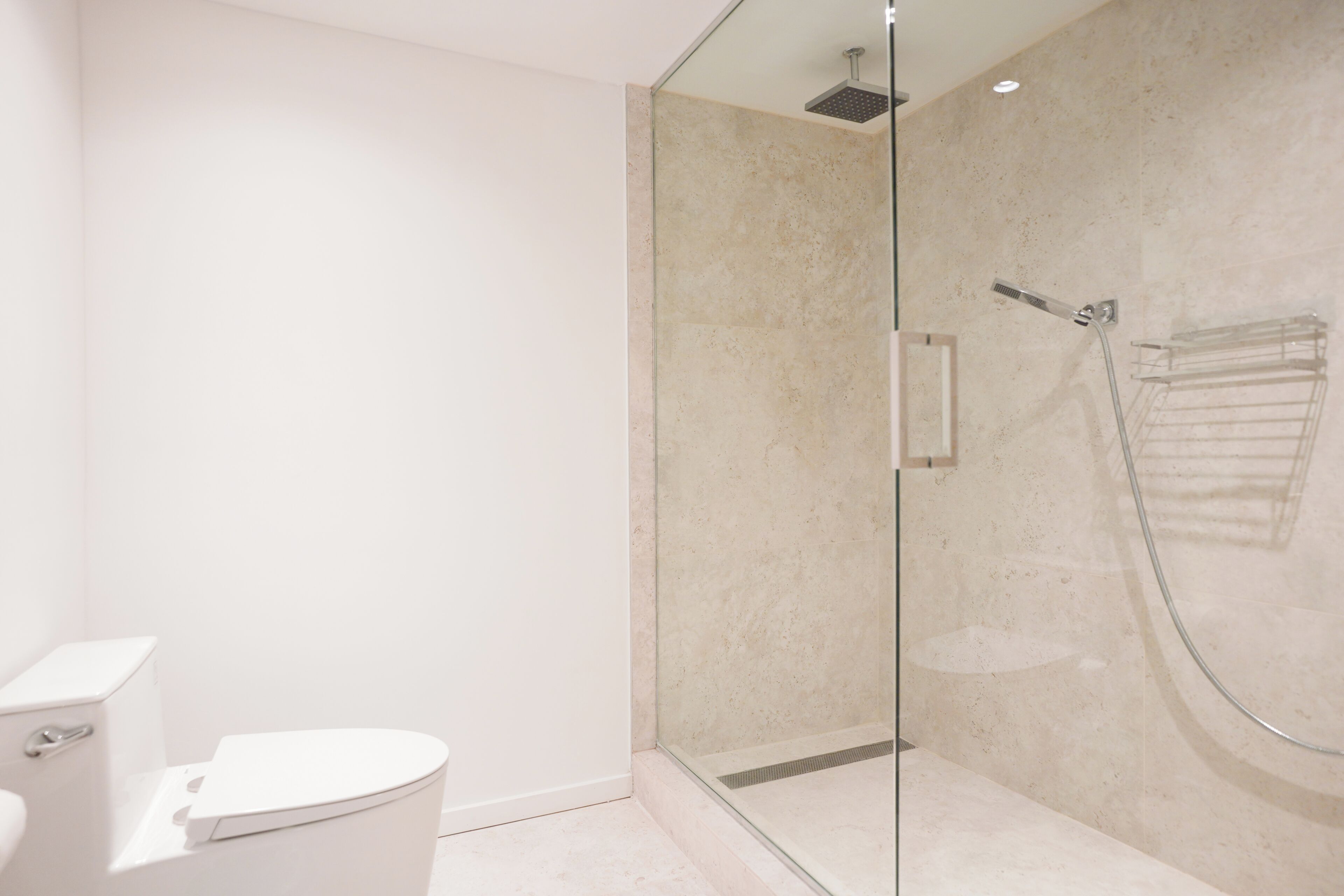 A modern bathroom with a glass-enclosed shower, a white toilet, and a beige tiled wall.