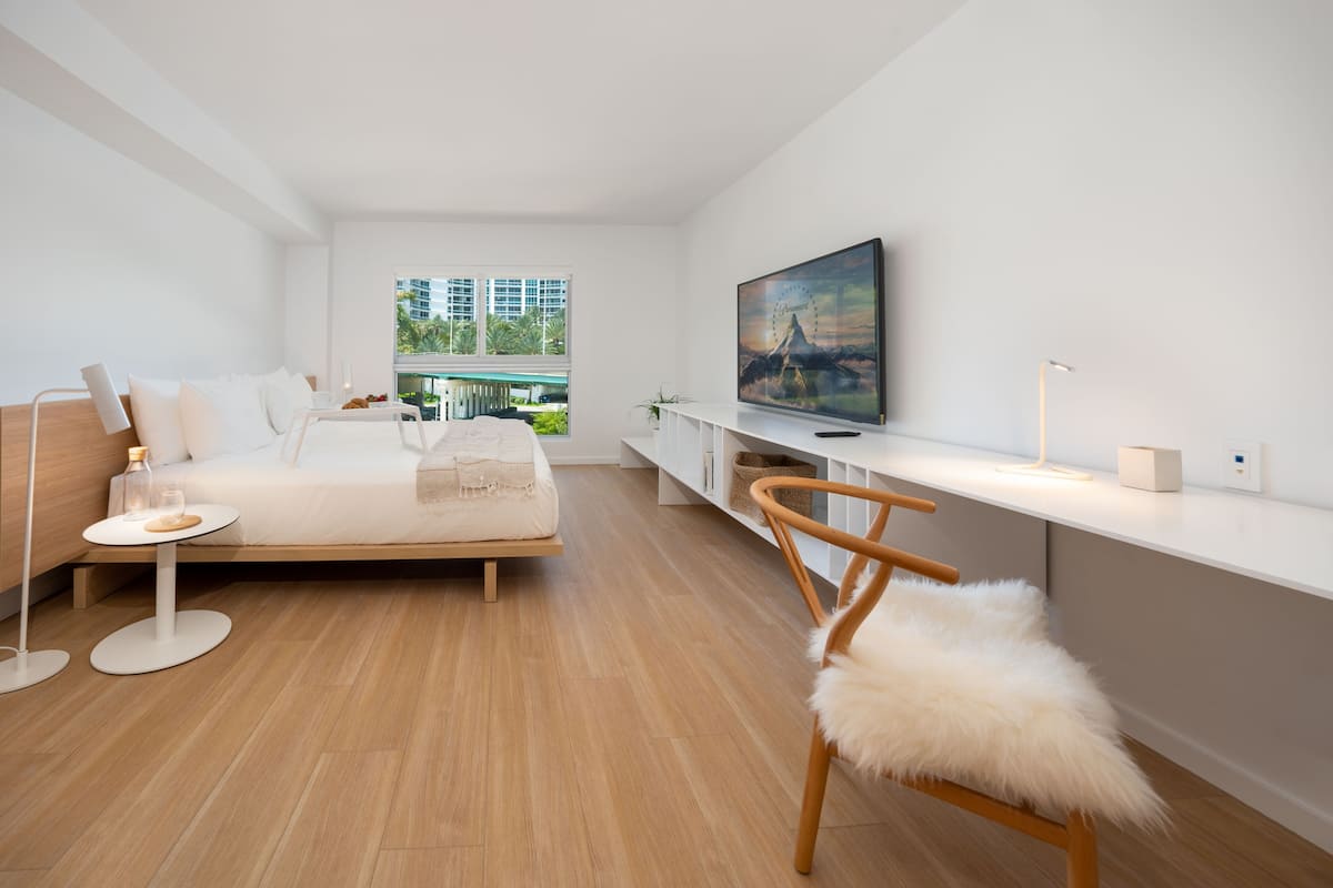 A modern bedroom with a bed, a TV, a desk, and a chair.