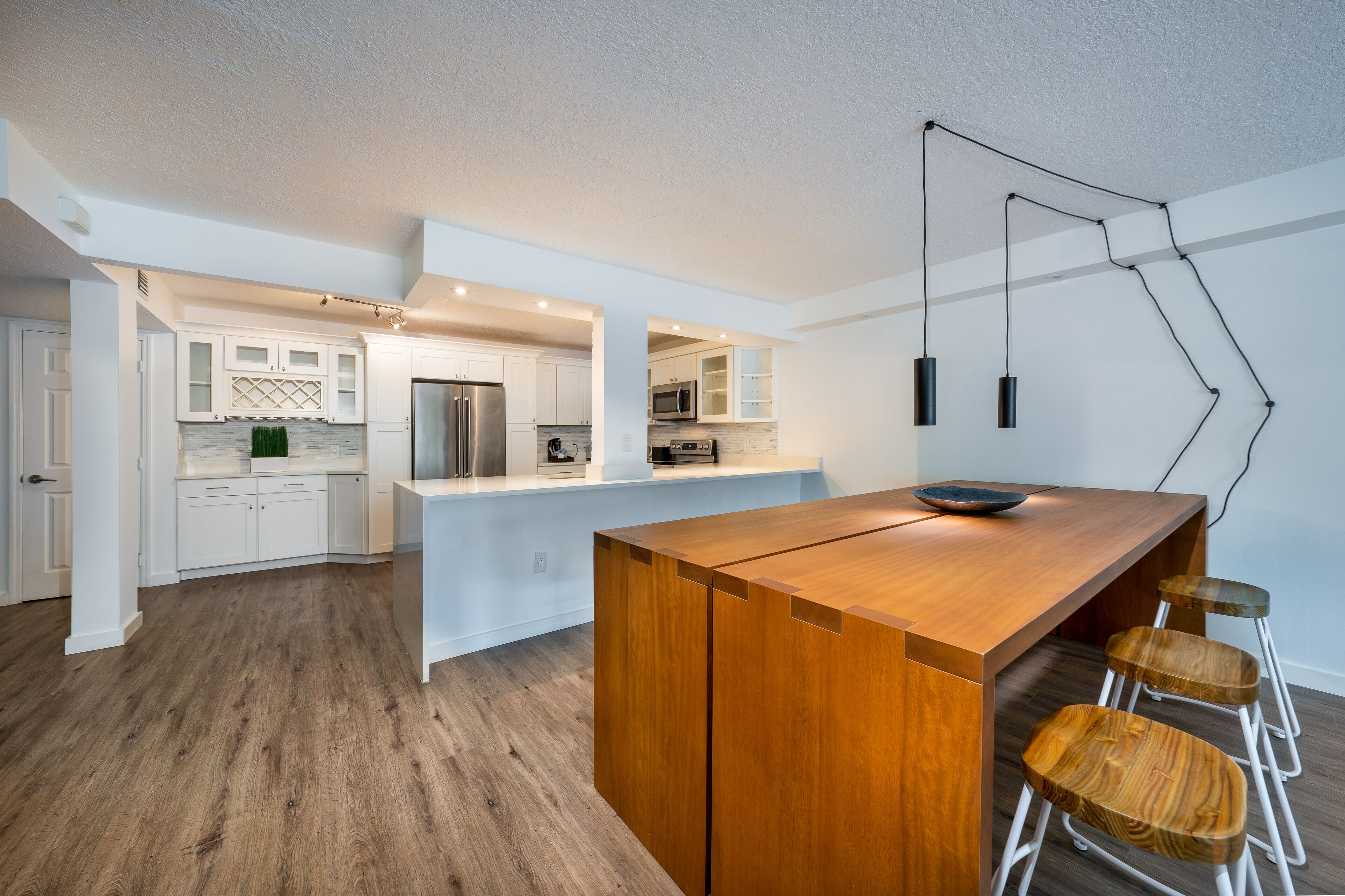 A modern kitchen with white cabinetry, a wooden island, and a bar area with stools.