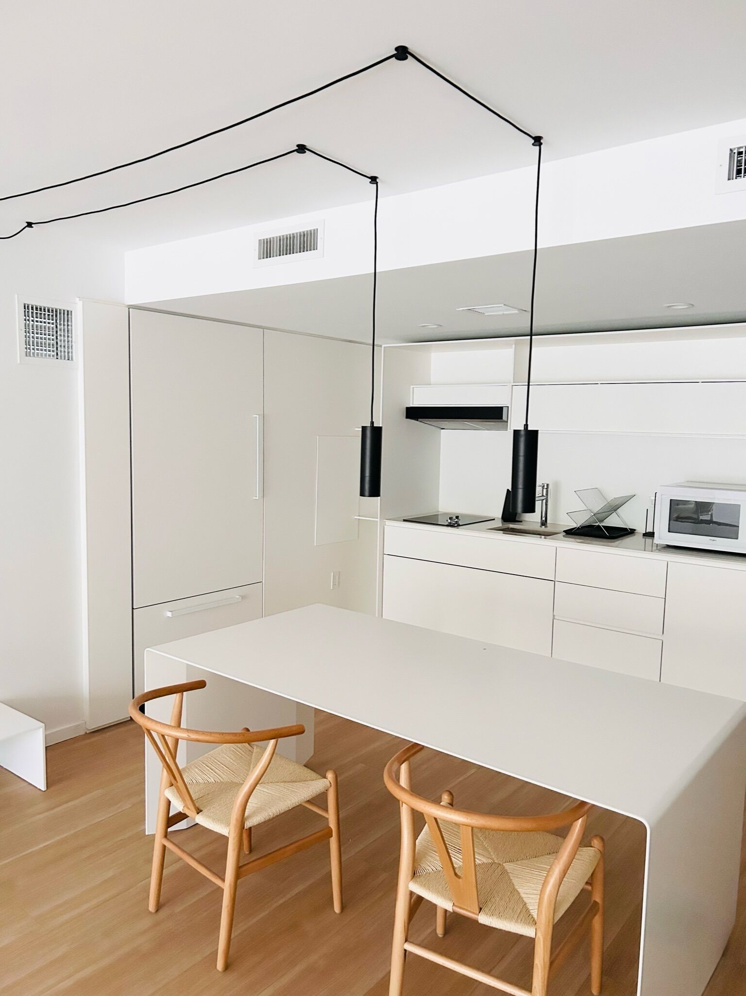 A modern kitchen with white cabinetry, a central island, two wooden chairs, and pendant lighting.