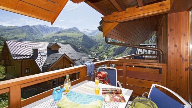 A wooden deck with a table, chairs, and a view of mountains.