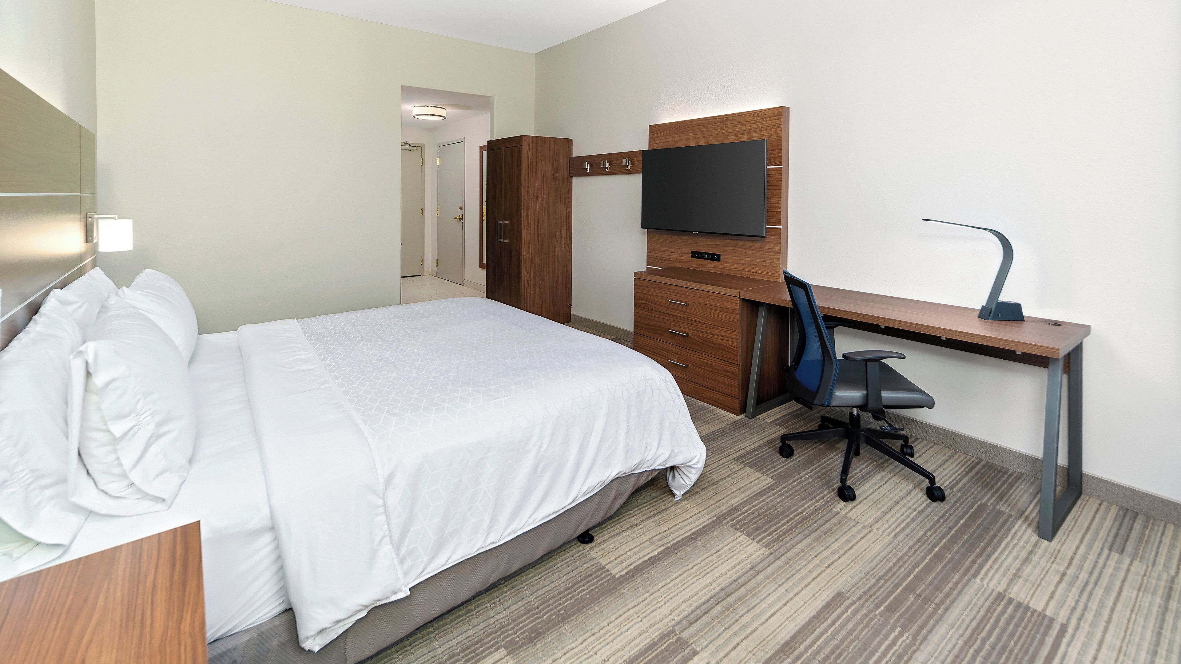 A hotel room with a bed, a desk with a computer, a chair, a TV, and a wardrobe.