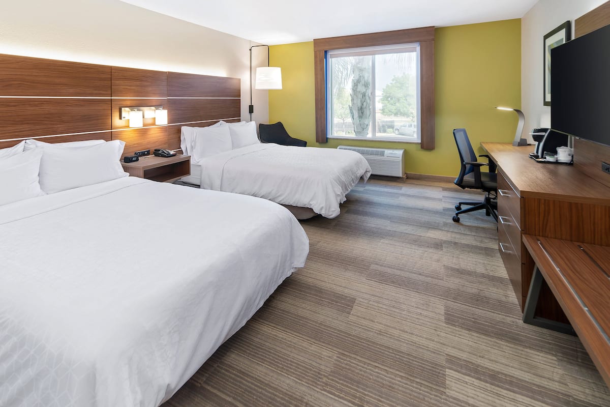 A hotel room with two beds, a desk, a chair, a TV, and a window with a view of the outside.