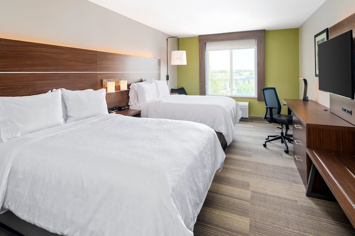A hotel room with two beds, a desk, a chair, a TV, and a window with a view.