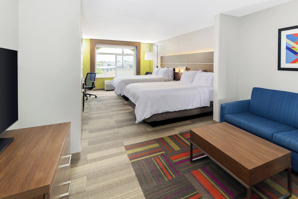 A hotel room with two beds, a blue sofa, a wooden coffee table, and a colorful rug.