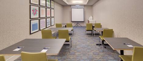 A conference room with tables and chairs, a projector screen, and framed artwork on the wall.
