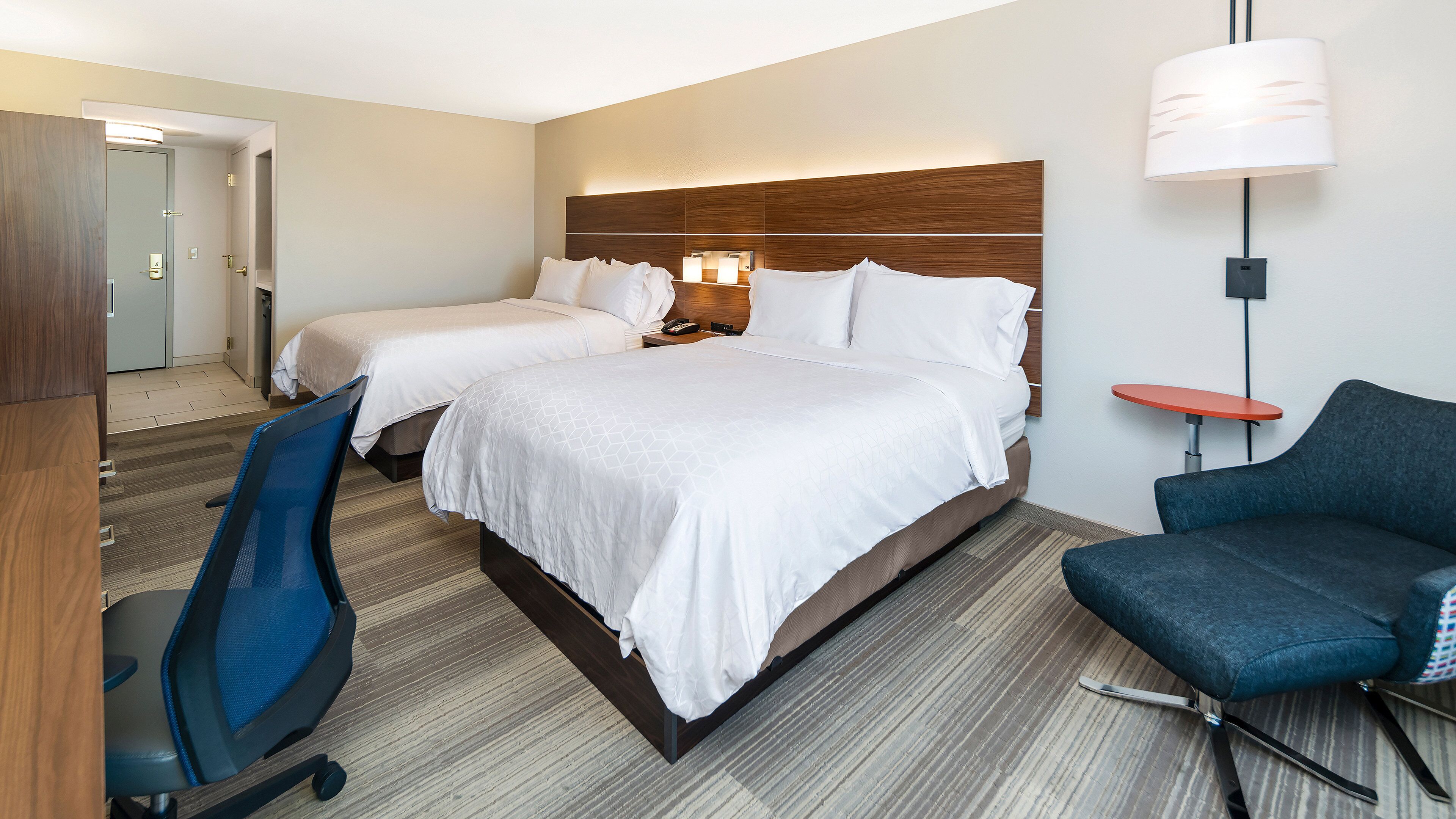 Une chambre d’hôtel avec deux lits, un bureau, une chaise et une lampe.