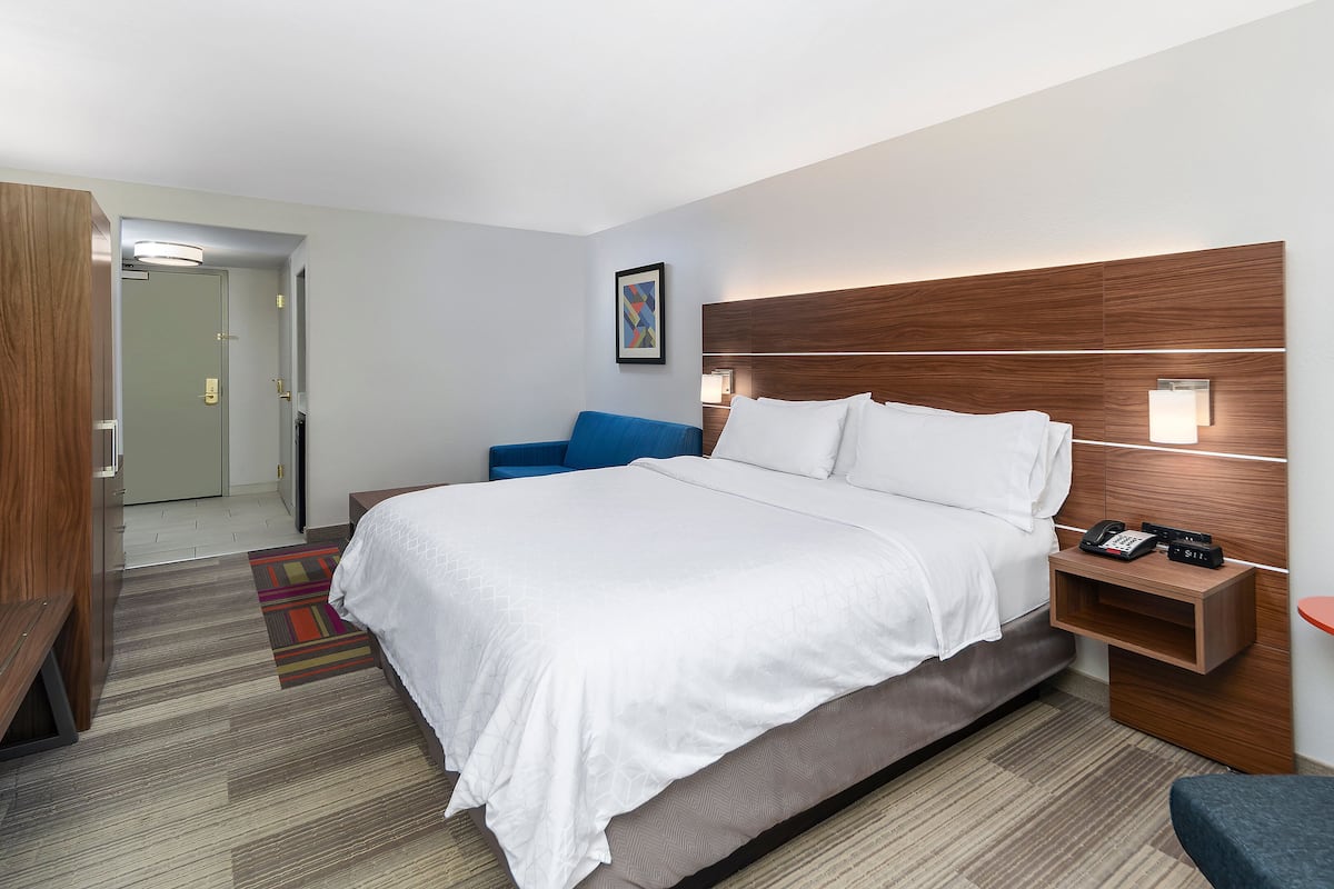 A hotel room with a large bed, a desk with a telephone, a chair, and a small table.