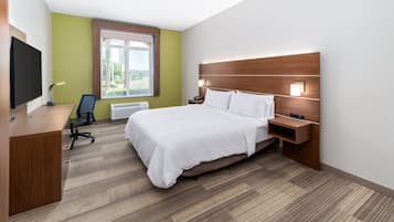 Habitación de hotel con cama, escritorio, silla, televisor, ventana y lámpara fijada a la pared.