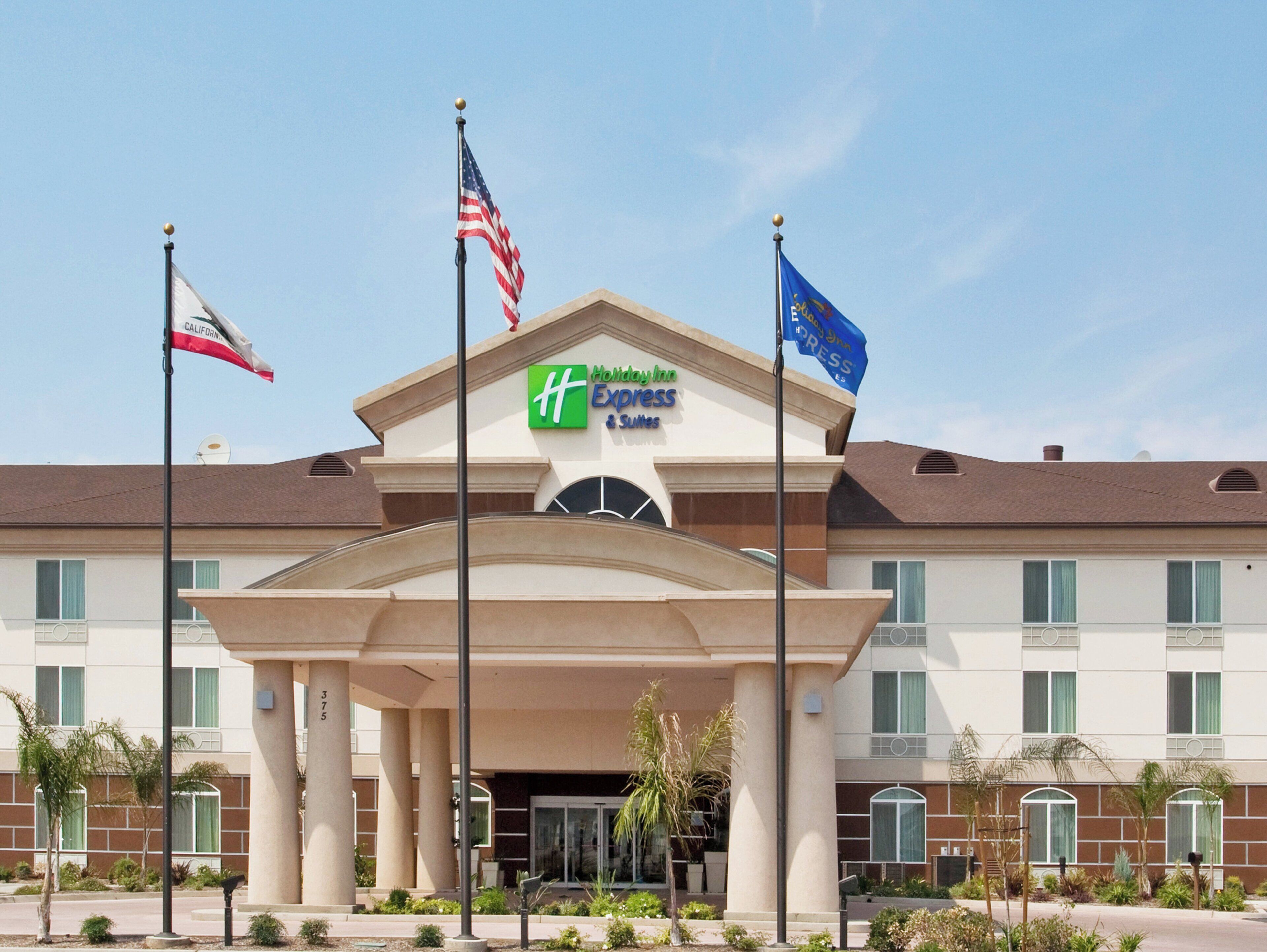 A hotel with a prominent 'Holiday Inn Express & Suites' sign, multiple flags, and a symmetrical facade with columns and a central entrance.